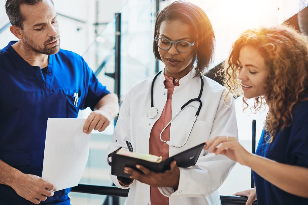 A group of healthcare professionals standing together in a hospital corridor in discussion looking at a book