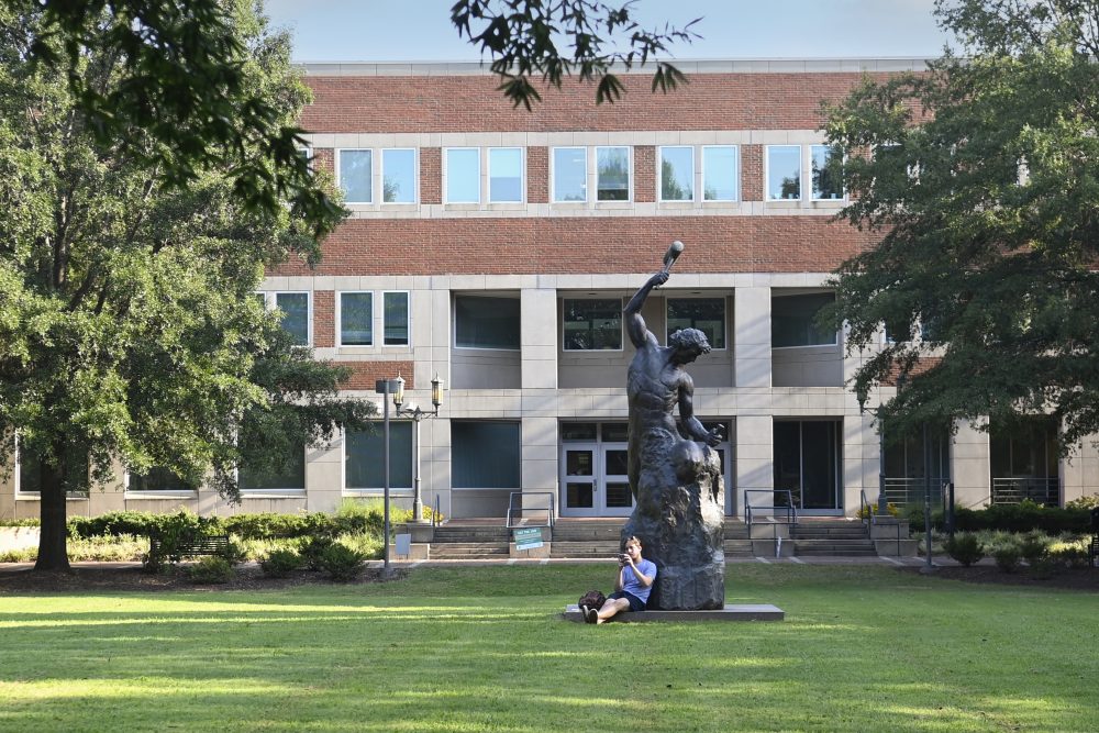 A student sits at the base of the Self-Made Man statue, in front of Fretwell on UNC Charlotte's main campus.
