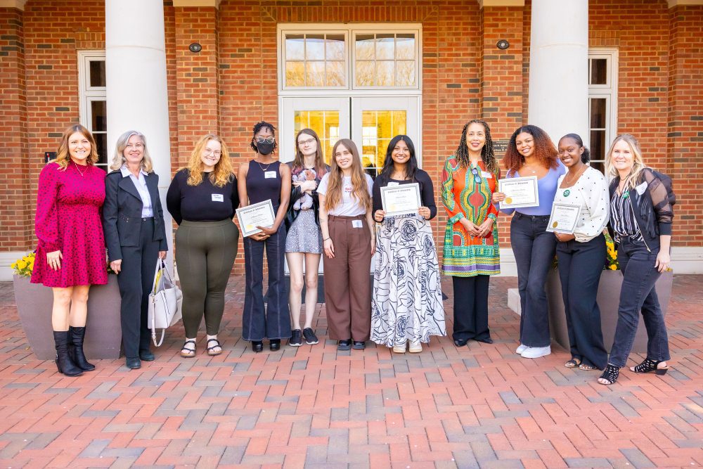 A group of people holding certificates in front of the UNC Charlotte Harris Alumni Center